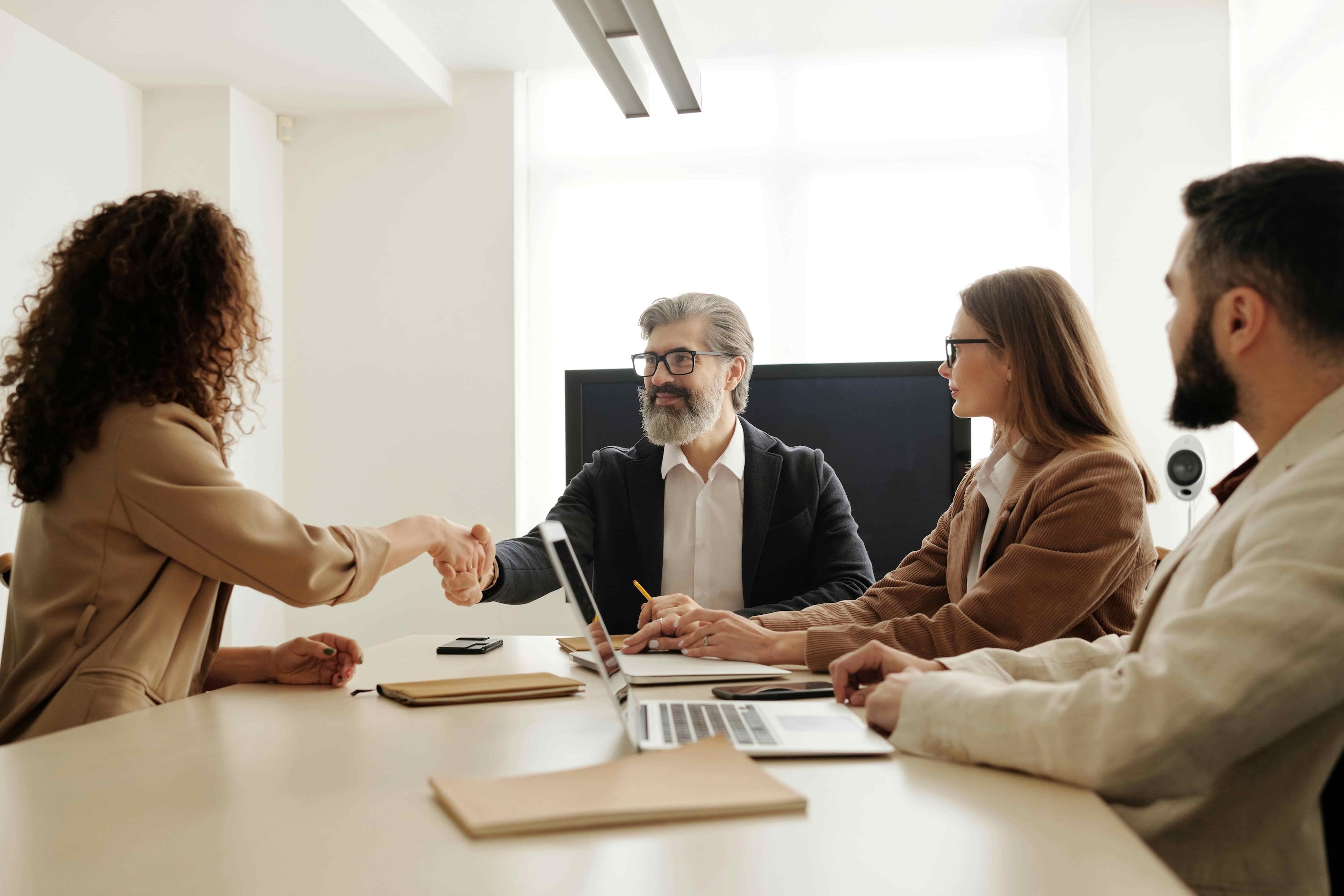 Group of people in a meeting setting with one person shaking hands.