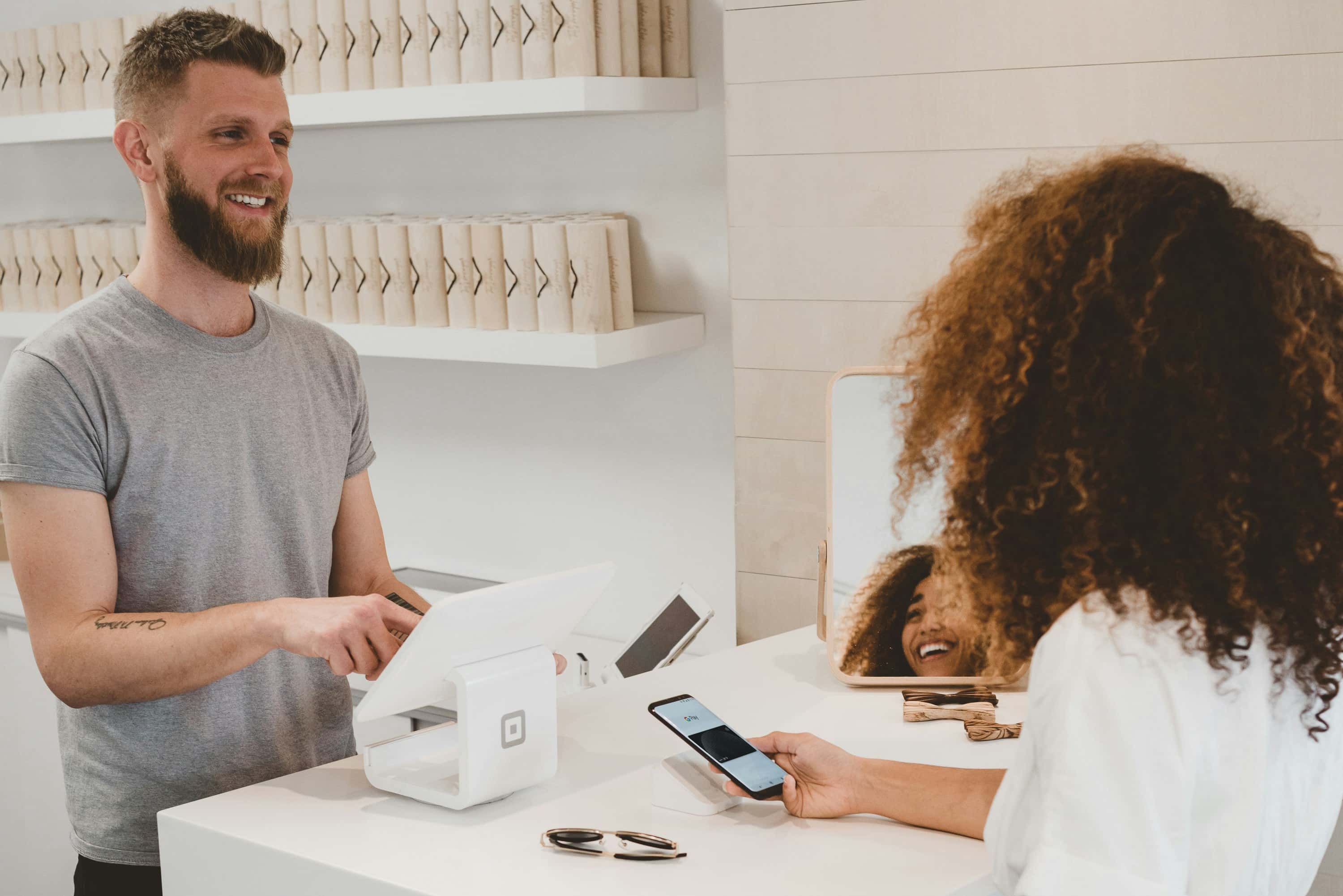 Woman using a smartphone at a counter making a payment at a small business.